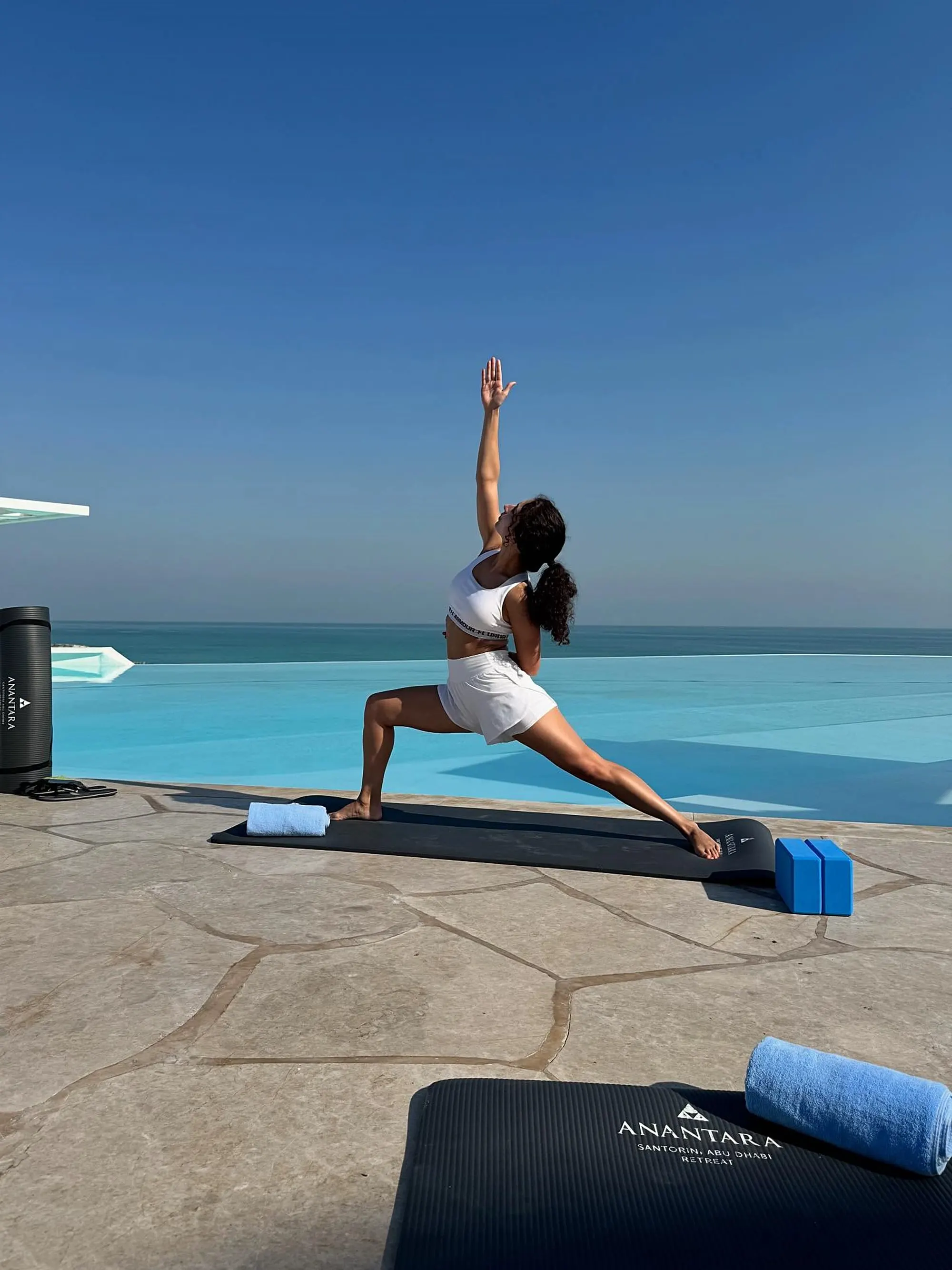 Teresa in a yoga reach pose on a sunny pool deck overlooking the sea